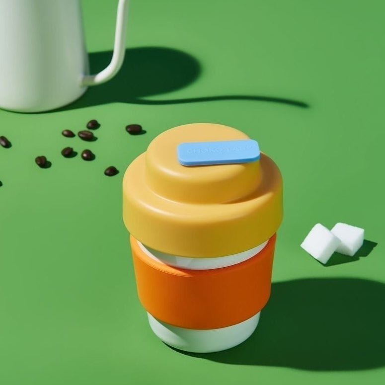 Gul och orange termosmugg mot grön bakgrund med kaffebönor